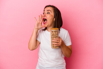 Middle age caucasian man holding a chickpeas jar isolated on pink background shouting and holding palm near opened mouth.