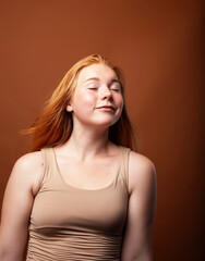 young pretty redhead girl posing cheerful on warm brown background, lifestyle people concept