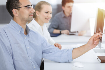 Fototapeta premium Business people working together in modern office. Happy smiling adult businessman using pc computer with colleagues. Teamwork and partnership concept