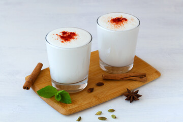 two glass Lassi drink with red pepper and fresh green mint on wooden board. cold dairy with spices: cinnamon and star anise. Indian cuisine. copy space. ayran, yogurt and probiotics on the white table