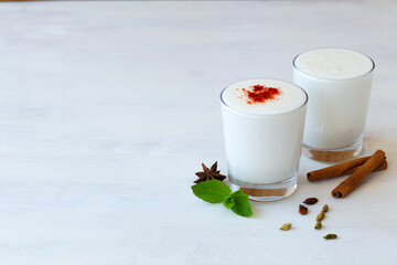 glass of milk.dessert, yogurt with probiotics on the table.Lassi drink with red pepper and fresh green mint on white. cold dairy with spices: cinnamon and star anise. Indian cuisine. copy space