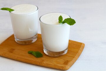 two glass of yogurt with green mint on wooden table. close-up fresh dairy drink.healthy, fermented products concept. Copy space.Kefir, milk or Lassi drink with probiotics on the table. Indian cuisine.