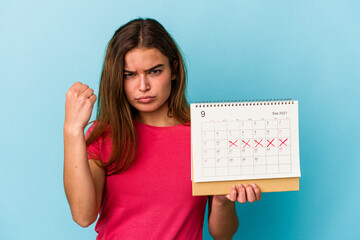 Young caucasian woman holding a calendar isolated on pink background showing fist to camera, aggressive facial expression.