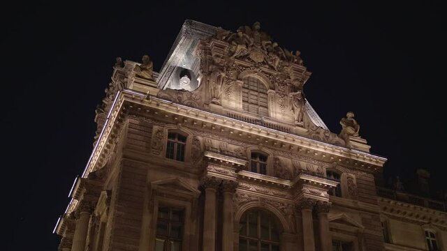 Historic building facade Mus&eacute;e du Louvre. Glide shot. Paris tourism attraction famous landmark. Romantic honeymoon travel destination. Glide shot in 4k. Close up view of Louvre building at night time.