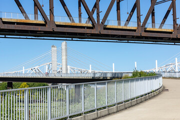 A pedestrian ramp leading to a pedestrian walk bridge over the Ohio River in Louisville, Kentucky with the Interstate 65 highway bridge in the background.