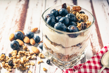 Normal view of a glass with a yogurt, blueberry and granola parfait on a rustic wooden table. Natural eating concept.