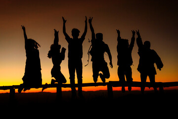 Obraz na płótnie Canvas silhouette Happy friends jumping on mountain peak at sunrise