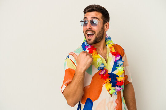 Fototapeta Young caucasian man dancing on a hawaiian party isolated on white background points with thumb finger away, laughing and carefree.