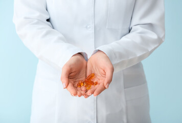 Female doctor holding fish oil pills on color background, closeup