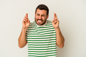 Young caucasian man isolated on white background crossing fingers for having luck