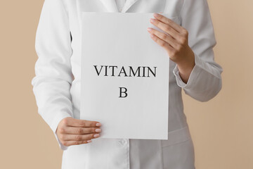 Female doctor holding sheet of paper with text VITAMIN B on color background, closeup