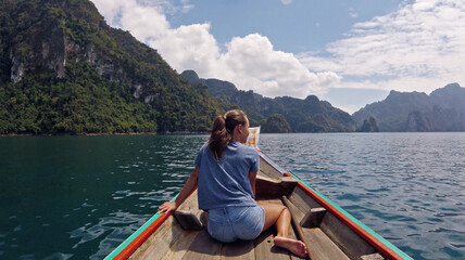 Fototapeta na wymiar Young Happy Mixed Race Girl Sitting and Relaxing on Traditional Thai Wooden Long Tail Boat at Khao Sok Lake. Phang Nga Province, Thailand.