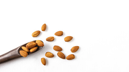 The almonds are in a brown wooden spoon and several seeds around which are on isolate a white background.