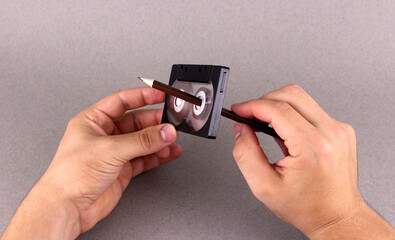Hand rewind audio cassette tape by pencil on gray background
