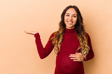 Young mexican pregnant woman isolated on beige background showing a copy space on a palm and...