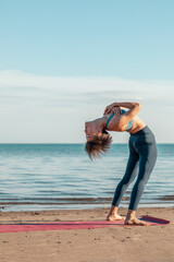 a young attractive woman, of Asian appearance, practicing yoga, performs a stretching exercise, on the beach