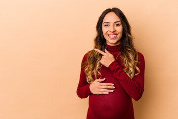 Young mexican pregnant woman isolated on beige background smiling and pointing aside, showing something at blank space.