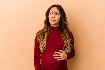 Fototapeta premium Young mexican pregnant woman isolated on beige background confused, feels doubtful and unsure.