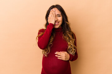 Fototapeta premium Young mexican pregnant woman isolated on beige background having fun covering half of face with palm.