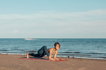 Fototapeta na wymiar a young attractive woman, of Asian appearance, practicing yoga, performs a stretching exercise, on the beach. the exercise Utthan Prishthasana,.the lizard pose