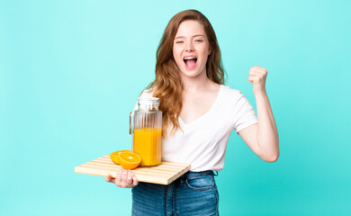 pretty red head woman shouting aggressively with an angry expression and holding an orange juice