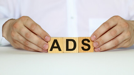 A businessman holds wooden cubes with a word ADS on a white background, with space to copy the text, business concept