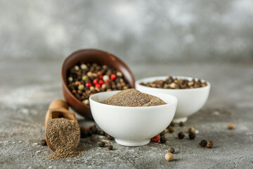 Bowls with black pepper powder and peppercorns on grunge background