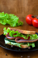 tasty sandwich with ham, green salad, cucumbers and tomatoes on the wooden background.toasted homemade sandwich with fresh vegetables on the black plate.copy space.vertical