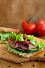 close up two tasty sandwiches with ham, green salad, cucumbers and tomatoes on the wooden background.toasted homemade sandwich with fresh vegetables on the brown cutting board.vertical.copy space