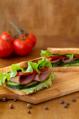 two tasty sandwiches with ham, green salad, cucumbers and tomatoes on the wooden background.toasted...