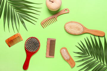 Hair brushes, combs and palm leaves on color background