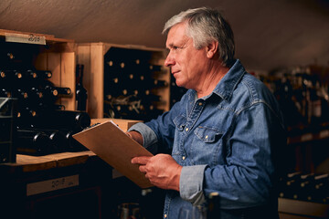 Winery worker counting the quantity of bottles left in cellar