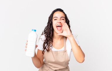 hispanic pretty chef woman feeling happy,giving a big shout out with hands next to mouth and holding a milk bottle
