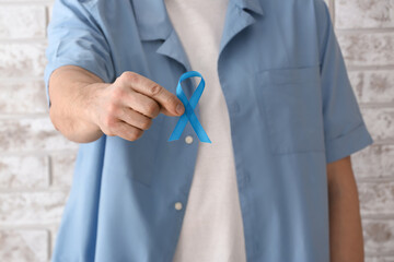 Man with blue ribbon near light brick wall, closeup. Prostate cancer concept