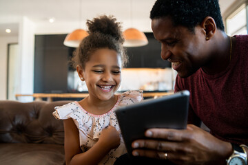 Father and daughter using digital tablet at home.