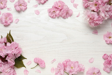 Beautiful frame of sakura tree blossoms on white wooden table, flat lay. Space for text