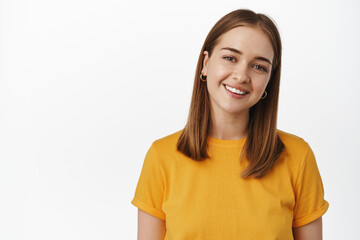 Portrait of candid young woman smiling white teeth, tilt head friendly and looking happy at camera, wearing yellow t-shirt against white background