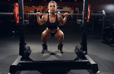 Strong female athlete doing squats with a barbell