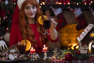 Pretty woman in Santa Claus hat near fireplace