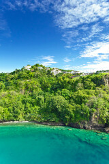 Fototapeta premium Coastline at Kingstown on Saint Vincent, steep cliff covered by trees behind turquoise and emerald colored water