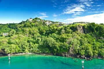 Coastline at Kingstown on Saint Vincent, steep cliff covered by trees behind turquoise and emerald...