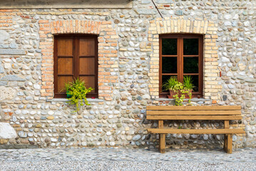 Fototapeta na wymiar Facciata di vecchia costruzione di pietra di recente ristrutturazione. Due finestre chiuse e una panca di legno. 