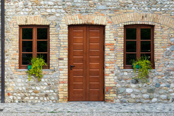 Facciata di vecchia casa ristrutturata con muro di pietra. Una porta di legno e due finestre chiuse. 