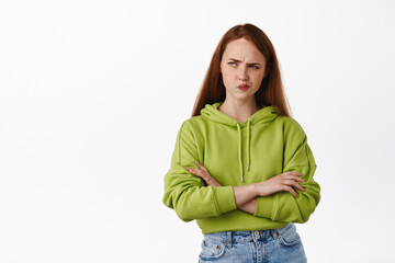 Complicated redhead girl looks puzzled, frowning and sulking while thinking, look aside and makes...