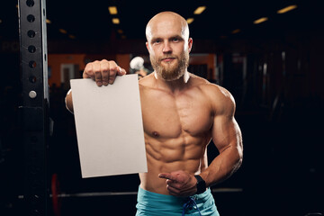 Shirtless athletic man holding a blank board at the gym