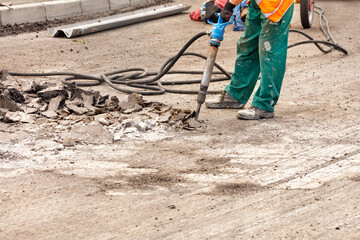 A road worker breaks up old asphalt with a pneumatic jackhammer on a stretch of road.