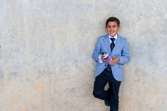 Stylish  boy in suit with can of paint Cheerful preteen Hispanic schoolboy in elegant suit and tie holding can of violet spray paint while standing against concrete wall