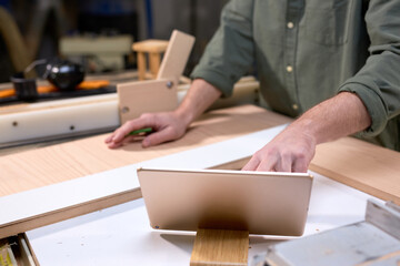 Close-up photo of male carpenter hands using digital tablet during work, work on project of making...