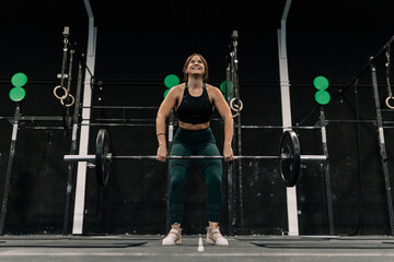 Fototapeta premium Young fitness woman doing barbell squats in a gym