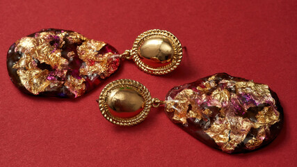 Close up shot of epoxy resin earrings with golden foil inside isolated over red background